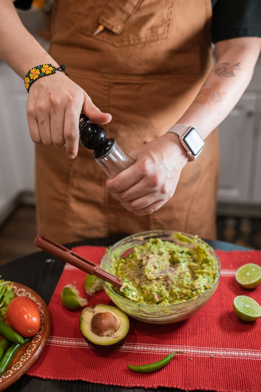 person in brown shirt holding black bottle pouring green vegetable on green vegetable salad