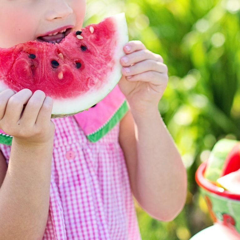 girl eating sliced watermelon fruit beside table